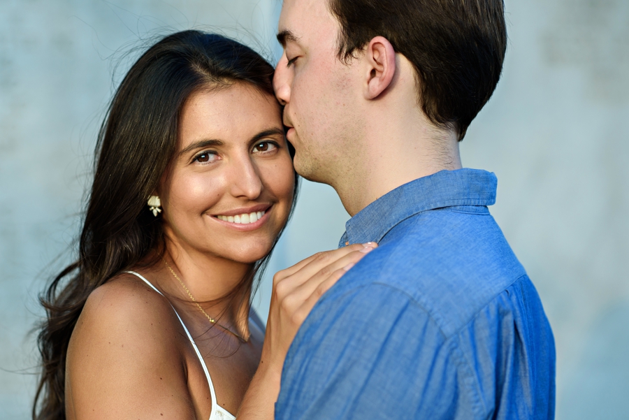 A groom to be holds his future bride and kisses her temple during their battery park engagement session.